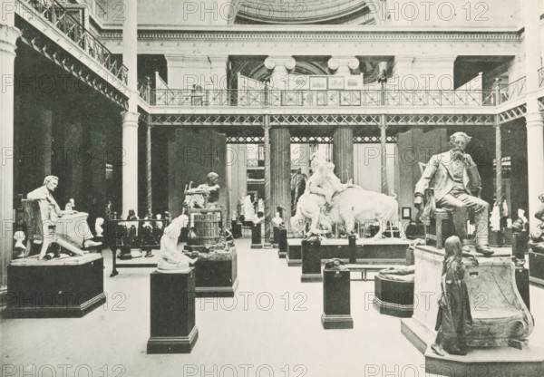 Interior of a room with sculptures in the Palace of Fine Arts at the World's Columbian Exposition in Chicago in 1893, Interior of Palace of Fine Arts, page, photomechanical print, number: 'Plate 61', photographer: Charles Dudley Arnold, Chicago, photographer: HD Higinbotham, cliché maker: anonymous, 1893, Charles Dudley Arnold, HD Higinbotham, photographer, clichémaker, North America, Illinois, paper, collotype, photoprint, height 134 mm x width 191 mm, piece of sculpture, reproduction of a piece of sculpture, permanent exhibition, museum, world fair, world exhibition, World's Columbian Exposition, Palace of Fine Arts, A large indoor gallery with high ceilings and a two-tiered iron and columned balcony running along the upper level, filled with numerous sculptures on pedestals and plinths arranged across the floor; visible statues include seated figures, a reclining animal with figures on its back, busts, and a standing figure in the foreground on a raised base.
