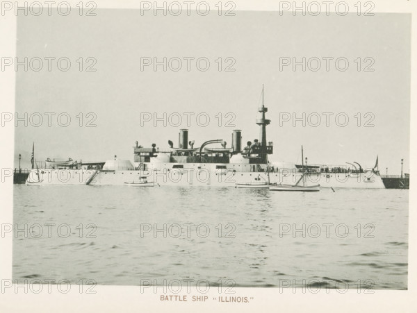 Battleship Illinois at the World's Columbian Exposition in Chicago in 1893, Battle ship 'Illinois', page, photomechanical print, number: 'Plate 69', photographer: Charles Dudley Arnold, Chicago, photographer: HD Higinbotham, cliché maker: anonymous, 1893, Charles Dudley Arnold, HD Higinbotham, photographer, cliché maker, North America, Illinois, paper, collotype, photoprint, height 133 mm x width 190 mm, ships (in general), world fair, world exhibition, World's Columbian Exposition, A large naval ship sits on calm water with a long low hull and multiple rounded turrets and openings along its side, a central superstructure with smokestacks and curved piping, a tall mast with platform near the top, and small boats floating nearby; people are visible on the ship's decks and near railings, flags fly at the bow and stern, and a pier extends behind the stern with lamp posts.