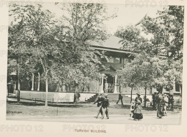 Pavilion of Turkey at the World's Columbian Exposition in Chicago in 1893, Turkish Building, page, photomechanical print, number: 'Plate 77', photographer: Charles Dudley Arnold, Chicago, photographer: HD Higinbotham, cliché maker: anonymous, 1893, Charles Dudley Arnold, HD Higinbotham, photographer, cliché maker, North America, Illinois, paper, collotype, light printing, height 130 mm x width 190 mm, world fair, world exhibition, World's Columbian Exposition, A large building partially obscured by numerous leafy trees sits behind a low wall with a series of steps leading up to a covered entrance; the building has ornate woodwork around the doorway and windowed panels along its facade, with a person standing in the entranceway. In the foreground several people walk along a path or street, including adults wearing long coats and hats and a child in a patterned dress, while others stand near the steps and a bicycle is visible near a group to the right.