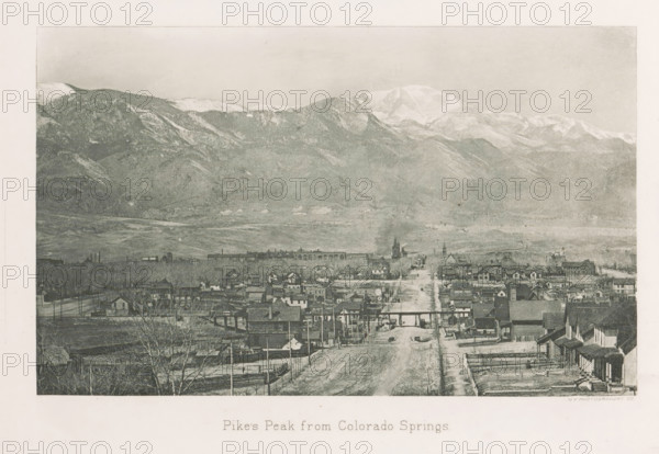 View of Colorado Springs and Pikes Peak, Pike's Peak from Colorado Springs, page, photomechanical print, photographer: WH Jackson Photograph and Publishing Co., Colorado Springs, cliché maker: New York Photo-Gravure Company, New York (city), c. 1888 - in or before 1893, WH Jackson Photograph and Publishing Co., New York Photo-Gravure Company, photographer, cliché maker, North America, Colorado, paper, photoaquatint, height 125 mm x width 202 mm, city-view in general, 'veduta', mountains, El Paso (Colorado), Pikes Peak (El Paso), A wide view shows a town street lined with wooden houses and small buildings leading toward a distant cluster of larger structures and church-like buildings, with a railroad bridge crossing the road and a couple of vehicles visible on the street; beyond the town there is a broad plain rising into rugged, forested foothills and then into a range of snow-capped mountains under a pale sky.