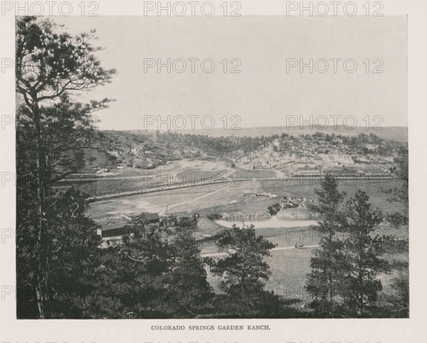 Landscape at Colorado Springs, Colorado Springs garden ranch, page, photomechanical print, Colorado Springs, cliché maker: New York Photo-Gravure Company, New York (city), c. 1888 - in or before 1893, photographer, North America, Colorado, paper, autotypie, height 155 mm x width 202 mm, landscapes, A grainy black and white landscape photograph showing a panoramic view from an elevated position with tall trees in the foreground on both sides, open fields and winding dirt paths below, scattered buildings and farm structures across the midground, a body of water with a small bridge or dam, rocky outcrops and wooded areas extending into the distance, and a wide pale sky occupying the upper portion of the image.