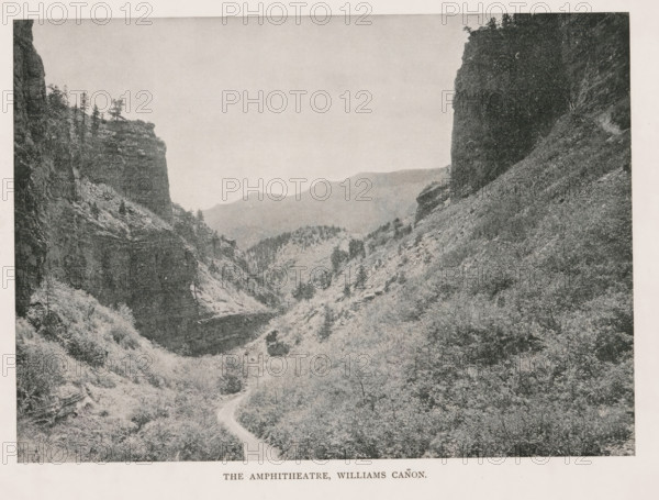 The Amphitheatre, Williams Cañon, View of the Williams Canyon, page, photomechanical print, Williams Canyon (El Paso, CO), cliché maker: New York Photo-Gravure Company, New York (city), c. 1888 - in or before 1893, photographer, North America, Colorado, El Paso (Colorado), paper, autotypie, height 146 mm x width 203 mm, landscapes, ravine, chasm, abyss, canyon, A high-contrast black-and-white landscape photograph showing a narrow winding dirt road leading into a deep canyon flanked by steep rocky cliffs and densely textured vegetation. The left side of the image features a tall cliff face with layered rock strata and a few sparse trees along its top edge, while the right side shows a darker, sheer rock wall descending to a slope covered in shrubs and underbrush. In the middle distance the canyon opens to reveal rolling ridges and tree-covered hills fading into a lighter-toned sky that occupies the upper portion of the image.