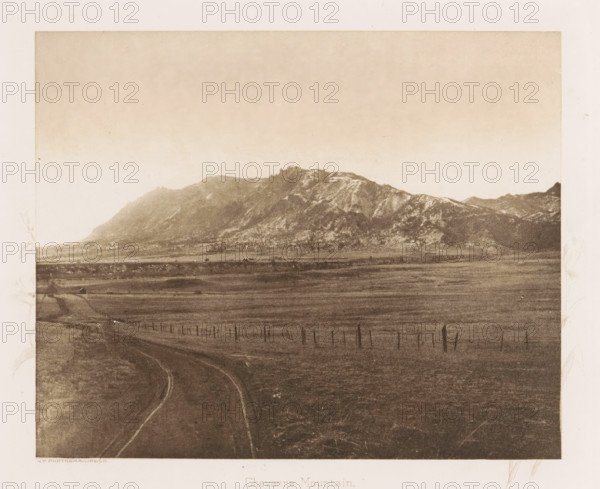 View of Cheyenne Mountain, Cheyenne Mountain, page, photomechanical print, photographer: WH Jackson Photograph and Publishing Co., Colorado, cliché maker: New York Photo-Gravure Company, New York (city), c. 1888 - in or before 1893, North America, paper, photoaquatint, height 144 mm x width 177 mm, landscapes, mountains, El Paso (Colorado), A sepia-toned landscape showing a broad plain in the foreground with a dirt road curving away toward the horizon, a line of posts and wire fences running parallel across the field, and a distant mountain range with rugged peaks and ridges under a pale sky.