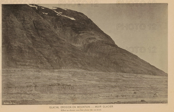 Glacial erosion on mountain, Muir Glacier, View of the glacial grooves of the Muir Glacier, page, photomechanical print, inscription: 'Effect as shown 1000 feet above the sea level.', inscription: 'Britton & Rey', cliché maker: Britton & Rey, New York (city), c. 1885 - in or before 1890, photographer, North America, Alaska, Skagway-Hoonah-Angoon, paper, collotype, photoprint, height 112 mm x width 185 mm, mountains, glacier, A wide, monochrome image of a steep, rocky mountainside with striated rock faces and patches of snow near the top, rising from a flat, layered foreground of textured terrain and sparse scattered rocks, under a blank sky.