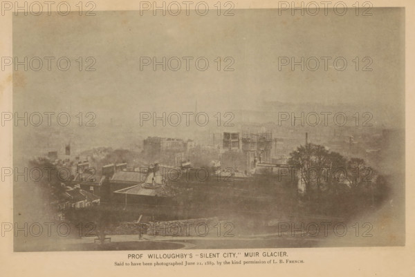 View of the imaginary city of Silent City in Alaska, Prof. Willoughby's Silent City, Muir Glacier, page, photomechanical print, inscription: 'Said to be photographed June 21, 1889, by the kind permission of LB French.', c. 1885 - in or before 1890, paper, collotype, photoprint, height 113 mm x width 184 mm, city-view in general, 'veduta', North America, Alaska, Skagway-Hoonah-Angoon, A faded, sepia-toned view of a cityscape seen from an elevated vantage, with rooftops and building facades in the foreground, several taller structures and a scaffolding-covered building toward the middle ground, and distant hazy buildings and a barely visible spire receding into a pale sky, with a cluster of leafed trees on the right and a low stone wall and a bench near the bottom edge.