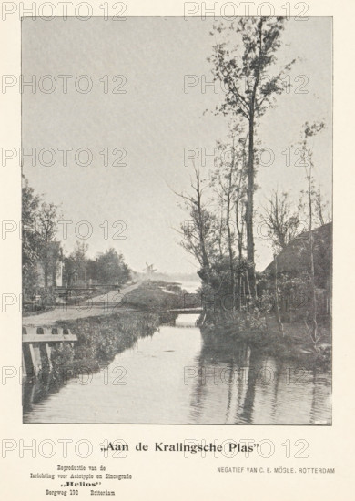 View of the Kralingse Plas, 'At the Kralingse Plas', page, photomechanical print, inscription: 'Reproduction of the, Establishment for Autotyping and Zincography, 'Helios', Bergweg 192 Rotterdam', photographer: Carl Emil Mögle, Rotterdam, cliché maker: Helios (Rotterdam) (possibly), c. 1895 - in or before 1900, printer (person), paper, autotypie, height 151 mm x width 114 mm, brook, Kralingse Plas, A vertical black-and-white photograph showing a narrow waterway running from the foreground toward the background, with reflections of tall, thin trees on the water surface. On the right bank a group of tall trees rises above a darker area of vegetation and a sloped structure partly visible behind them. The left bank shows low grassy edges, a wooden railing or fence near the foreground, and additional trees and small structures receding into the distance. A distant windmill silhouette is visible on the horizon where the waterway narrows, and the sky above is largely clear. The image is borde...
