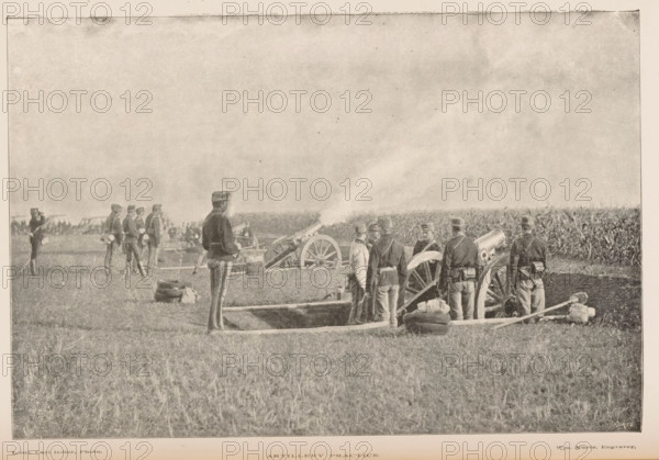 Military exercise with artillery, Artillery practice, page, photomechanical print, inscription: 'Kurtz', photographer: Carl Hiller, cliché maker: Kurtz, 1887 - 1907, paper, autotypie, height 115 mm x width 171 mm, artillery range, firing range, shooting range, military training, warfare, military affairs, A group of uniformed men stand in a grassy field around large wheeled cannons with smoke emerging from one barrel, some men facing the artillery and others turned slightly away, with sacks and equipment on the ground near shallow dugouts; in the background more figures and distant lines of vegetation are visible under a wide sky.