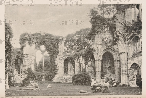 Ruins of Velton Abbey, View of the ruins of Velton Abbey, page, photomechanical print, photographer: Mansell, cliché maker: Photochrome Engraving Co., New York (city), 1887 - 1907, North America, paper, autotypie, height 113 mm x width 166 mm, landscape with ruins, A sepia-toned photograph shows the stone ruins of a large arched structure with tall columns and vaulted openings, parts of the walls broken and overgrown with vegetation. Trees and dense foliage grow among and above the ruins, with ivy covering some stone surfaces. On the grass in front of the arches a group of people in period clothing sit and recline, some wearing hats, while scattered stones and low masonry remain on the lawn. The sky above is pale and open, and the overall scene has a weathered, aged appearance.