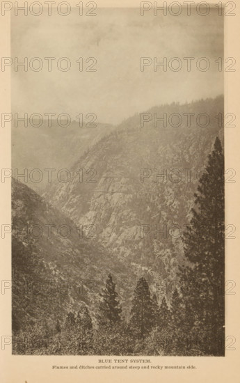 Blue Tent System, View of the Blue Tent mining settlement near Nevada, California, page, photomechanical print, inscription: 'Flumes and ditches carried around steep and rocky mountain side.', Nevada, c. 1885 - in or before 1890, North America, paper, collotype, photogravure, height 184 mm x width 112 mm, Print on third unnumbered page after page 122., mountains, mine, A vertical sepia-toned photograph of a steep rocky mountainside with rugged cliffs and scattered trees, showing a deep valley between ridges and a line of conifer trees rising along the slopes, with a large solitary tree silhouette on the right edge and a hazy sky above.