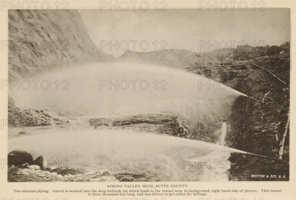 View of Spring Valley Mine in Butte County, California, Spring Valley Mine, Butte County, page, photomechanical print, inscription: 'Two streams piping. Gravel is washed into the deep bedrock cut which leads to the tunnel seen in background, right hand side of picture. This tunnel, is three thousand feet long, and was driven to get outlet for tailings.', maker: Britton & Rey, c. 1885 - in or before 1890, North America, paper, collotype, photoprint, height 112 mm x width 183 mm, mine, A sepia-toned landscape photograph showing steep rocky cliffs on both sides of a wide, misty plume of water or spray arcing across the scene from the right toward the left, with rough rocky terrain and scattered boulders visible beneath and around the plume, a narrow ledge or path along the right cliff with some wooden structures or rails, distant low hills visible through the mist in the background, and a light border surrounding the image.