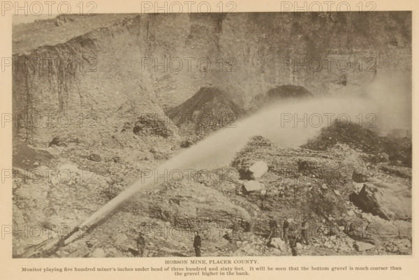 View of Hobson Mine in Placer County, California, Hobson Mine, Placer County, page, photomechanical print, inscription: 'Monitor playing five hundred miner's inches under head of three hundred and sixty feet. It will be seen that the bottom gravel is much coarser than, the gravel higher in the bank.', c. 1885 - in or before 1890, North America, paper, collotype, photoprint, height 111 mm x width 183 mm, mine, A sepia-toned photograph shows a rocky hillside with steep exposed soil and vertical streaks on the cliff face, loose rubble and piles of gravel scattered across the slope, a large arcing spray of water originating from a pipe or nozzle near the lower left and extending toward the upper right where mist obscures part of the terrain, several men standing and working among the rocks near the bottom edge, and scattered larger rocks and boulders among finer debris.