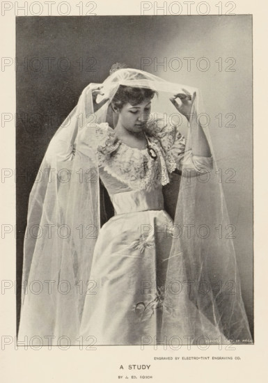 A study, page, photomechanical print, photographer: J. Ed. Rosch, cliché maker: Electro-Tint Engraving Co., c. 1890 - in or before 1895, paper, autotypie, height 150 mm x width 108 mm, bride (in wedding dress), A woman wearing a formal gown with puffed sleeves and decorative lace on the bodice is shown adjusting a long translucent veil draped over her head and shoulders, her gaze directed downward, one hand lifting the veil near her forehead and the other holding it at the side, the skirt of the gown falling smoothly with a subtle floral embellishment, and a plain dark background framed within a lighter border.