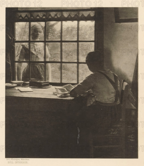 Woman doing needlework at a table and another woman looking in through the window, Holl. Interior, page, photomechanical print, photographer: LL Kleintjes, Netherlands (possibly), clichémaker: anonymous, c. 1898 - in or before 1903, paper, photoaquatint, height 169 mm x width 148 mm, Print fourteen of fourteen prints at the back of the book., adult woman, sewing, closed window, A dim interior scene shows a person seated at a wooden table near a paned window, seen from behind with short hair and suspenders, hands resting on or near folded cloth on the tabletop, with plates and a stack of rectangular objects on the table; outside the window a standing figure wearing a head covering and a dress is visible through the glass panes, framed by the window grid and a patterned valance at the top, with soft, muted lighting and a plain wall to the right.