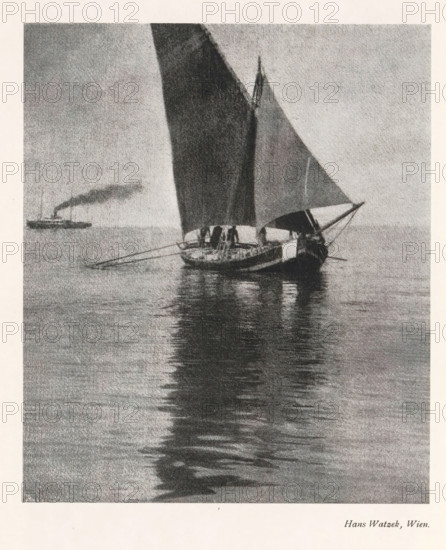 Sailing ship on open water, page, photomechanical print, photographer: Hans Watzek, cliché maker: Meisenbach, Riffarth & Cie. (possibly), Berlin, c. 1898 - in or before 1903, paper, autotypie, height 164 mm x width 139 mm, Print on third unnumbered page after page 160., sailing-ship, sailing-boat, sea (seascape), A grayscale image of a sailboat on calm water with two tall sails raised and their reflection visible on the water, a small crew or figures on the deck, a long horizontal boat structure with oars extending outward, gentle ripples across the water, and a distant vessel emitting a plume of dark smoke on the horizon.