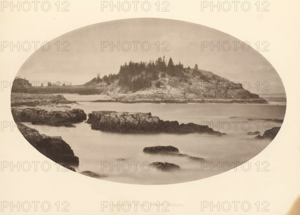 View of Schooner Head on Mount Desert Island, Maine, Schooner Head, Mount Desert, page, photomechanical print, c. 1875 - in or before 1880, North America, Mount Desert Island, paper, collotype, photoprint, height 115 mm x width 190 mm, cape (coast), A sepia-toned oval photograph depicting a rocky coastline with a foreground of dark jagged rocks partially submerged in smooth, misty water, a midground of larger rocky outcrops rising from the water, and a tree-covered promontory with dense conifer silhouettes along its ridge, a low shoreline stretching toward the left where a small building sits near the edge, and a pale sky filling the upper portion of the frame.