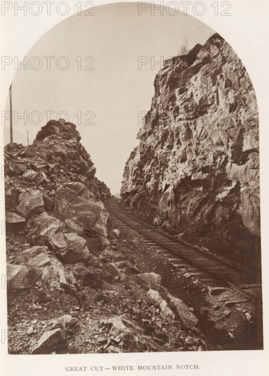 Great Cut - White Mountain Notch, View of a train track along White Mountain Notch, New Hampshire, page, photomechanical print, White Mountains, c. 1874 - in or before 1879, North America, paper, collotype, photoprint, height 173 mm, width 127 mm, Print for chapter 6., railway, train, mountains, A sepia-toned photograph showing a narrow railroad track running between two steep, rocky cliffs, with jagged rock faces and scattered boulders on the ground, the rails curving away into the distance, a tall wooden post visible near the left cliff, and sparse vegetation or small shrubs atop the cliffs under a pale sky.