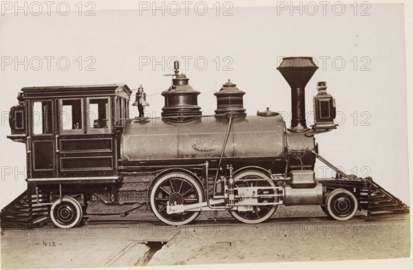 American steam locomotive, photograph, page, United States of America, c. 1871 - in or before 1881, photographer, North America, paper, albumen print, height 124 mm x width 200 mm, Photo on page 136., steam locomotive, A sepia-toned side view of an old steam locomotive showing the cab with paneled wooden sides and window openings, a rounded boiler with riveted seams and decorative trim, and large spoked driving wheels with visible connecting rods and mechanical linkages. Two domed fittings sit atop the boiler, one with a bell mounted beside it and a slender vertical whistle or valve. A tall, flared smokestack rises near the front with a rectangular lamp mounted to its side. The locomotive rests on wooden rails and a dirt surface with a small open trench visible beneath the track.