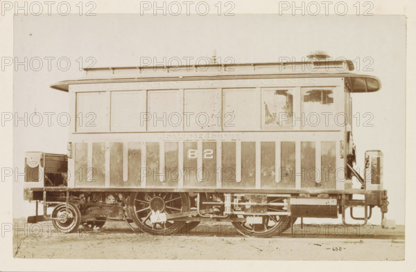 American passenger steam locomotive, photograph, page, United States of America, c. 1871 - in or before 1881, photographer, North America, paper, albumen print, height 124 mm x width 199 mm, Photo on page 150., steam locomotive, A sepia-toned photograph of a railway car shown from the side, with a rectangular body featuring vertical panels along the lower half and a row of larger rectangular sections above, a rounded overhanging roof with a small vent or dome on top, a window with partially peeled material on one side, metal wheels and visible mechanical undercarriage components, platform ends with railings and a small step, and the image framed by a lighter border.