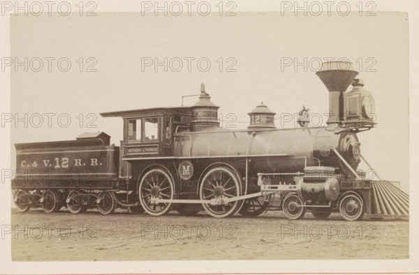 American passenger and freight steam locomotive, photograph, page, United States of America, c. 1871 - in or before 1881, photographer, North America, paper, albumen print, height 124 mm x width 199 mm, Photo on page 68., steam locomotive, A vintage steam locomotive and its attached coal car sit on flat ground, shown in a side view across the image. The locomotive has a tall funnel-shaped smokestack, a large round headlight housing at the front, a cowcatcher with angled slats, two large driving wheels with visible spokes and connecting rods, cylindrical tanks and domes along the boiler, a cab with windows and a roof overhang, and decorative round emblems on the wheels and boiler. The coal car behind the engine has a rectangular open-top shape and visible wheelsets beneath. The scene is in sepia tones and the background is plain and light, with the ground in front appearing textured and slightly uneven.