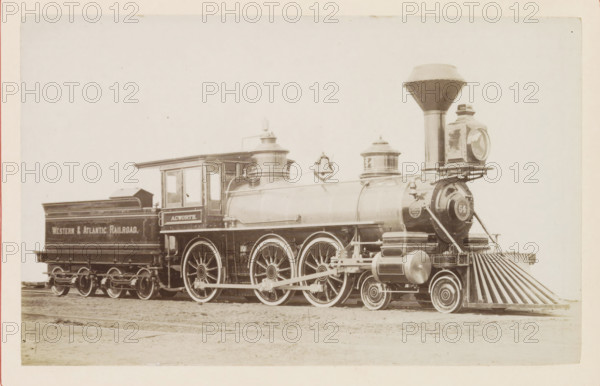 American freight steam locomotive, photograph, page, United States of America, c. 1871 - in or before 1881, photographer, North America, paper, albumen print, height 125 mm x width 198 mm, Photo on page 84., steam locomotive, A sepia-toned photograph of a vintage steam locomotive positioned on tracks, showing the engine and its attached coal car. The locomotive has a tall, flared smokestack and a large round headlamp mounted at the front above a slatted pilot. Two cylindrical domes sit along the top of the boiler, and a bell hangs between them. The cab has windows and a roof overhang, and the coal car behind it has a raised rear section. Large spoked driving wheels and smaller leading wheels are visible, with connecting rods and mechanical linkages along the side. The surface beneath the train appears to be dirt, and the background is a pale, empty sky. The image border shows a thin margin around the photograph.