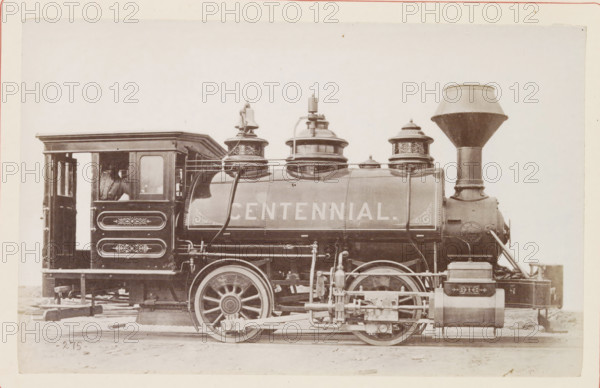 American steam locomotive, photograph, page, number: '275', United States of America, c. 1871 - in or before 1881, photographer, North America, paper, albumen print, height 124 mm x width 200 mm, Photo on page 118., steam locomotive, A sepia-toned image of a vintage steam locomotive viewed from the side, showing a rectangular cab with an open doorway and a window, decorative paneling on the cab side, a cylindrical boiler with ornate domes and piping on top, large spoked driving wheels with visible connecting rods and mechanical linkages, a tall funnel-shaped smokestack at the front, various tanks and external fittings along the lower side, and part of a wooden platform beneath the locomotive.