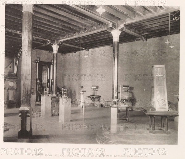 Room for electrical and magnetic measurements, photograph, page, photographer: Edward H. Hart, United States Naval Academy, cliché maker: The Photo-gravure Co., New York (city), c. 1885 - in or before 1890, North America, Maryland, Annapolis, paper, collotype, photoprint, height 185 mm x width 233 mm, laboratory, research room, military academy, A large interior space with exposed wooden ceiling beams supported by square and round columns with decorative capitals, brick walls, hanging light fixtures, several worktables and pedestals holding mechanical instruments and machines, a tall wooden cabinet leaning against a wall, stairs and a doorway partially visible in the background, and various cables and small equipment on the floor.