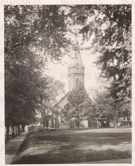 Chapel, photograph, page, photographer: Edward H. Hart, United States Naval Academy, cliché maker: The Photo-gravure Co., New York (city), c. 1885 - in or before 1890, North America, Maryland, Annapolis, paper, collotype, photoprint, height 231 mm x width 183 mm, facade (of house or building), church (exterior) - QQ - small church, military academy, A tall church steeple with a cross at its peak rises above a building partially obscured by dense trees, with the steeple's brick tower and arched window visible through branches; large leafy trees frame the scene on both sides and cast dappled shadows across a grassy foreground and a paved walkway that runs along the left edge, while light filters through the canopy creating patches of brightness on the lawn.