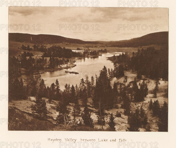 Hayden Valley between lake and falls, page, photomechanical print, photographer: Frank Jay Haynes, Yellowstone National Park, cliché maker: The Photo-gravure Co., New York (city), c. 1882 - in or before 1887, North America, paper, photoaquatint, height 162 mm x width 212 mm, dale, valley, Hayden Valley, A sepia-toned landscape photograph showing a wide river winding through a valley with forested hills on both sides; the foreground contains a slope dotted with numerous trees and patches of bare ground, the river reflects light and narrows toward the distant center of the image, clusters of trees and small islands appear along the riverbanks, rolling hills and wooded ridgelines form the middle and background under a sky with faint cloud patterns.