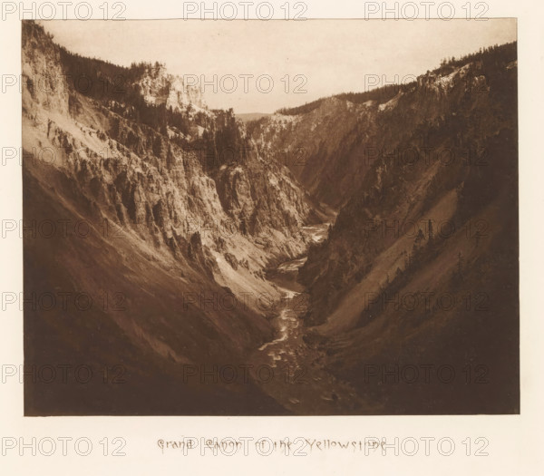 Grand Canyon of the Yellowstone, page, photomechanical print, photographer: Frank Jay Haynes, Yellowstone National Park, cliché maker: The Photo-gravure Co., New York (city), c. 1882 - in or before 1887, North America, paper, photoaquatint, height 165 mm x width 208 mm, river, ravine, chasm, abyss, canyon, Grand Canyon (Yellowstone National Park), A sepia-toned photograph shows a deep canyon with steep rocky walls and jagged cliffs descending to a narrow river winding through the canyon floor, with sparse trees and patches of vegetation clinging to the slopes and ridgelines under a pale sky.