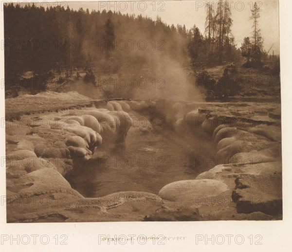 Crater of Oblong Geyser, page, photomechanical print, photographer: Frank Jay Haynes, Yellowstone National Park, cliché maker: The Photo-gravure Co., New York (city), c. 1882 - in or before 1887, North America, paper, photoaquatint, height 166 mm x width 210 mm, hot spring, geyser, A sepia-toned landscape showing a steaming geothermal pool set in a rocky basin with rounded, bulbous rock formations along the edges and a narrow channel of water leading inward, steam rising from the center and drifting upward, a distant tree-lined ridge with tall conifer silhouettes forming the backdrop, and a rugged foreground of textured mineral deposits and eroded rock surfaces.