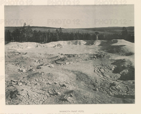 Mammoth paint pots, page, photomechanical print, photographer: Frank Jay Haynes, Yellowstone National Park, cliché maker: The Photo-gravure Co., New York (city), c. 1886 - in or before 1891, North America, paper, collotype, photoprint, height 165 mm x width 215 mm, pound, pool, Fountain Paint Pot, A wide grayscale landscape showing cracked and textured ground in the foreground that slopes toward a rimmed basin with pale, uneven mounds and a shallow pool, a dark treeline along the horizon behind the basin, and two small figures standing near the basin edge with one holding a dark umbrella.