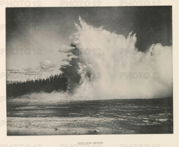 Excelsior geyser, page, photomechanical print, photographer: Frank Jay Haynes, Yellowstone National Park, cliché maker: The Photo-gravure Co., New York (city), c. 1886 - in or before 1891, North America, paper, collotype, photoprint, height 165 mm x width 215 mm, hot spring, geyser, A wide landscape photograph in grayscale showing a large, towering plume of steam or mist rising dramatically from the right side, with textured billowing edges and varying tones from light to dark; a dark treeline silhouette sits low on the horizon beneath the plume, and a flat foreground of textured ground and shallow ripples extends toward the viewer under a darkened sky.