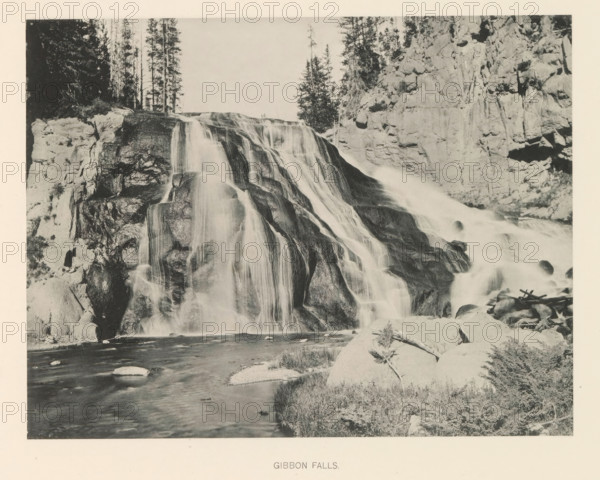 Gibbon Falls, page, photomechanical print, photographer: Frank Jay Haynes, Yellowstone National Park, cliché maker: The Photo-gravure Co., New York (city), c. 1886 - in or before 1891, North America, paper, collotype, photoprint, height 165 mm x width 216 mm, river, A wide waterfall cascades over layered rock ledges, the water appearing smooth as it flows down dark, rounded stones into a river below; steep rocky cliffs flank the falls on both sides, and tall, slender trees rise above the cliff edge at the top; in the foreground a rocky riverbank with scattered boulders and low vegetation borders the flowing water.
