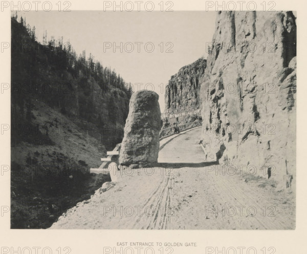 East entrance to Golden Gate, page, photomechanical print, photographer: Frank Jay Haynes, Yellowstone National Park, cliché maker: The Photo-gravure Co., New York (city), c. 1886 - in or before 1891, North America, paper, collotype, photoprint, height 165 mm x width 215 mm, public road, A narrow dirt road curves between steep rock walls with a wooden railing along its outer edge, a large rounded boulder sits near the road’s inner side, tall rocky cliffs rise on either side with rough textured surfaces, a figure appears seated on the railing partway along the road, tire tracks are visible in the dirt, distant trees grow on the ridge of the left cliff, and the sky above is clear.
