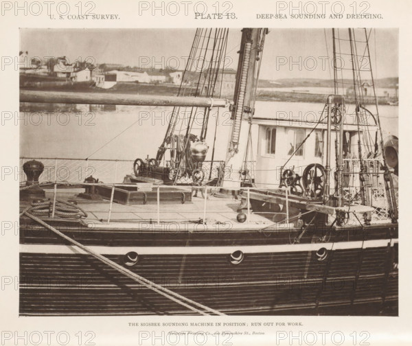 View of the Sigsbee sounding machine on the George S. Blake, page, photomechanical print, inscription: 'The Sigsbee sounding machine in position: run out for work.', name: 'Heliotype Printing Co., 220 Devonshire St., Boston.', number: 'Plate 13.', United States of America, printer (person): Heliotype Printing Company, Boston (Massachusetts), c. 1870 - in or before 1880, printer (person), North America, Massachusetts, paper, collotype, photoprint, height 158 mm x width 208 mm, steamship, motorship, machines, parts of machines, tools and appliances, fathoming, sounding, A sepia-toned photograph showing the deck and side of a wooden ship with visible rigging, masts, coiled ropes, pulleys, winches, and metal fittings, alongside a small deckhouse with windows and a railing; in the background across the water there are low buildings and shoreline features.