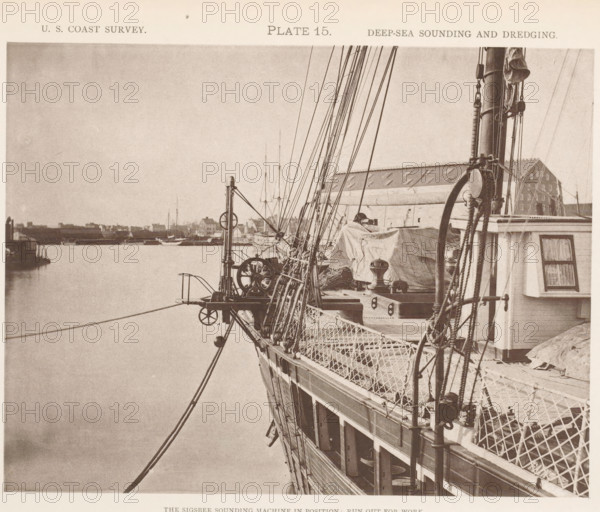 View of the Sigsbee sounding machine at the George S. Blake, page, photomechanical print, inscription: 'The Sigsbee sounding machine in position: run out for work.', number: 'Plate 15.', name: 'Heliotype Printing Co., 220 Devonshire St., Boston.', United States of America, printer (person): Heliotype Printing Company, Boston (Massachusetts), c. 1870 - in or before 1880, printer (person), North America, Massachusetts, paper, collotype, photoprint, height 165 mm x width 215 mm, steamship, motorship, machines, parts of machines, tools and appliances, fathoming, sounding, A sepia-toned photograph showing the side and deck of a sailing vessel with ropes, rigging, pulleys, and netted railings, a covered area on deck with tarpaulin and mechanical winches, a tall mast with additional rigging and a coiled rope, a small cabin window with curtains, and a calm body of water alongside a distant shoreline with low buildings and moored boats visible on the horizon.