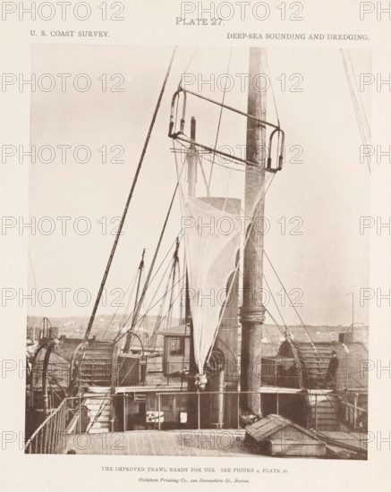 View of a trawl on the deck of the George S. Blake, page, photomechanical print, number: 'Plate 27.', inscription: 'The improved trawl ready for use. See figure 2, plate 26.', name: 'Heliotype Printing Co., 220 Devonshire St., Boston.', United States of America, printer (person): Heliotype Printing Company, Boston (Massachusetts), c. 1870 - in or before 1880, printer (person), North America, Massachusetts, paper, collotype, photoprint, height 197 mm x width 164 mm, fishing net, ships (in general), A sepia-toned photograph of a ship deck showing a large vertical mast with rigging and a suspended net hanging down from a horizontal frame attached near the top of the mast, with ropes and pulleys running to various points on the deck. The deck area shows wooden planking, railings, and mechanical winches or drums on either side, with ladders, cabins, and structural elements partially visible. In the background there are distant shoreline features and additional masts and spars rising above t...