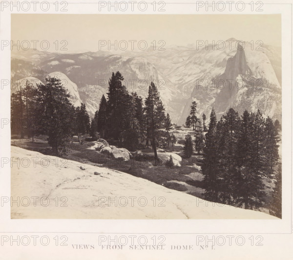View of the Yosemite Valley from Sentinel Dome, Views from Sentinel Dome No. 1, photograph, page, number: 'XIX.', photographer: Carleton E. Watkins, Yosemite Valley, c. 1860 - in or before 1868, North America, California, paper, albumen print, height 156 mm x width 206 mm, mountains, rock-formations, dale, valley, A wide sepia-toned landscape photograph showing a mountainous scene with a foreground of a rounded rocky slope and scattered boulders, a midground populated by clusters of tall evergreen trees and open grassy patches, and a distant backdrop of layered mountain ridges and steep granite cliffs with a prominent sheer rock face rising on the right side, all under a pale sky.