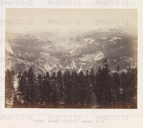 View of the Yosemite Valley from Sentinel Dome, Views from Sentinel Dome No. 2, photograph, page, number: 'XX.', photographer: Carleton E. Watkins, Yosemite Valley, c. 1860 - in or before 1868, North America, California, paper, albumen print, height 156 mm x width 206 mm, mountains, rock-formations, dale, valley, A wide sepia-toned landscape photograph showing a mountainous valley scene with snow-dusted peaks and rounded granite domes receding into a hazy sky, steep rocky cliffs and ridges forming layered slopes across the middle distance, a waterfall cascading down a sheer rock face near the center, and a dense foreground of tall evergreen trees partially covering lower rock formations.