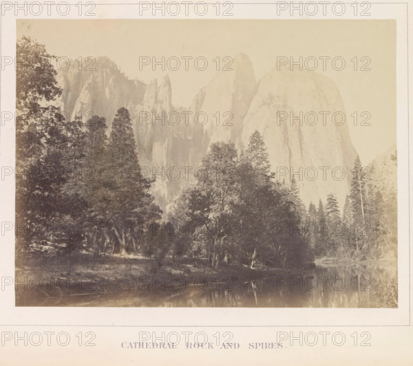 View of Middle Cathedral Rock and other spiers in the Yosemite Valley, Cathedral Rock ans Spires, photograph, page, number: 'VI.', photographer: Carleton E. Watkins, Yosemite Valley, c. 1860 - in or before 1868, North America, California, paper, albumen print, height 155 mm x width 206 mm, mountains, rock-formations, dale, valley, A sepia-toned landscape photograph showing tall rocky cliffs and spires rising behind a dense stand of trees, with a variety of tree silhouettes in the foreground and a calm reflective body of water along the lower edge, all framed by a pale border.