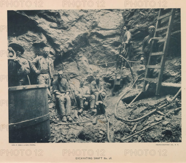 Excavating shaft No. 26, page, photomechanical print, photographer: Hall & Son, George P., New York, cliché maker: The Photo-gravure Co., c. 1883 - in or before 1887, North America, paper, collotype, photoprint, height 352 mm x width 281 mm, Print on frontispiece., working class, labourers, digging (industrial process), shafts and galleries (of a mine), A sepia-toned photograph shows a rocky excavation with a rough rock wall as the background and a group of workers standing and sitting on rubble in the foreground, some wearing hats and work clothes and some with tool marks and dirt on their faces and hands; a wooden ladder leans against the rock on the right side and a tripod-mounted mechanical drill or hoisting device stands near the center, surrounded by chains, hoses, and scattered hand tools resting on the ground and on rocks.