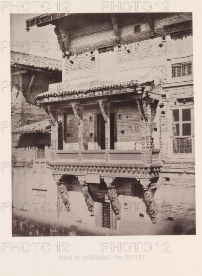 Façade of a house with a balcony in Ahmedabad, Gujarat, India, page, photomechanical print, title: 'HOUSE AT AHMEDABAD, 17TH CENTURY.', number: 'II.', Ahmedabad (city), maker: Heliotype Printing Company, Boston (Massachusetts), c. 1875 - in or before 1885, photographer, North America, Massachusetts, paper, photoaquatint, height 230 mm x width 189 mm, urban housing, balcony, façade (of house or building), A sepia photograph of a brick building facade featuring a carved wooden balcony with ornate columns and decorative brackets, a tiled roof edge with a hanging ornament, rectangular windows with barred grilles, and a textured brick surface with various holes and repairs.