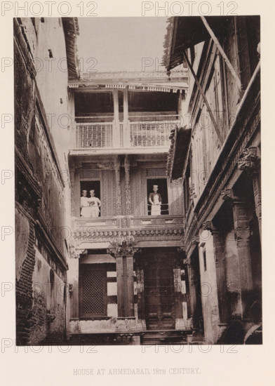 View of a house with three men in Ahmedabad, Gujarat, India, page, photomechanical print, number: 'III.', title: 'HOUSE AT AHMEDABAD, 18TH CENTURY.', Ahmedabad (city), maker: Heliotype Printing Company, Boston (Massachusetts), c. 1875 - in or before 1885, photographer, North America, Massachusetts, paper, photoaquatint, height 233 mm x width 174 mm, urban housing, facade (of house or building), A narrow courtyard framed by tall, ornate walls and balconies, showing intricately carved wooden columns and decorative latticework; three people stand at the upper level, two grouped together at one opening and one at a separate opening, all leaning on the balcony railings; the facade displays patterned panels, carved brackets, and a large central doorway with a grid-covered window beside it; the opposite side shows layered wooden beams and supports with visible wear and textured walls.