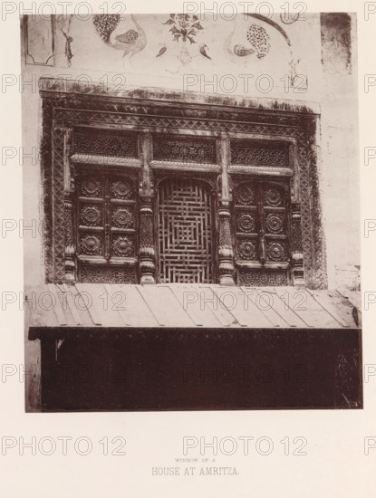 View of a window with ornaments in Amritsar, Punjab, India, page, photomechanical print, title: 'WINDOW OF A, HOUSE AT AMRITZA.', number: 'IX.', Amritsar, maker: Heliotype Printing Company, Boston (Massachusetts), c. 1875 - in or before 1885, photographer, North America, Massachusetts, paper, photoaquatint, height 210 mm x width 179 mm, anthropomorphic ornament, window, A photographic image of an ornate wooden window set into a wall, showing carved panels with floral rosette motifs and geometric latticework, fluted columns and decorative borders framing the window, a painted frieze above with bird and floral designs, a sloped metal awning below with visible seams, and a dark recessed opening beneath the awning.
