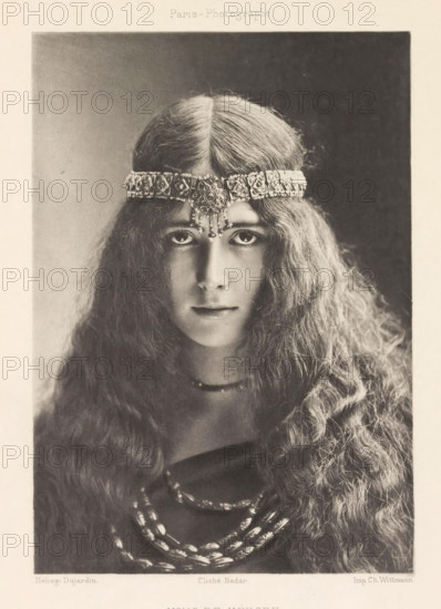 Portrait of Cléo de Mérode, Melle de Mérode de l'Opéra, page, photomechanical print, photographer: Félix Nadar, Paris, cliché maker: Dujardin, France, printer (person): Charles Wittmann, c. 1884 - in or before 1894, Félix Nadar, Dujardin, Charles Wittmann, photographer, cliché maker, printer (person), paper, photoaquatint, height 158 mm x width 111 mm, Person, Cléo de Mérode, portrait of actor, actress, A sepia-toned portrait of a young person with long, wavy hair parting down the middle, wearing an ornate jeweled headband that rests across the forehead and features a central pendant with small dangling ornaments; the face is shown frontally with large, dark eyes looking forward, a straight nose, and closed lips; a simple necklace sits at the throat and multiple beaded strands drape over a dark garment; the background is plain and darker at the top, fading toward the sides.