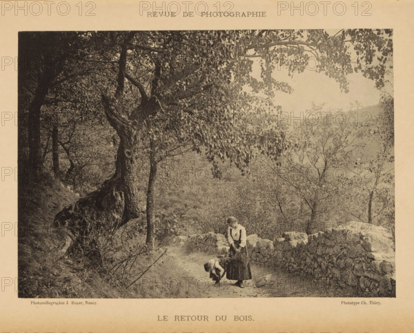 Le redactie du bois, Two unknown young women on a path near a forest, page, photomechanical print, maker: Jules Royer, maker: C. Thiry, c. 1887 - in or before 1892, paper, collotype, photoprint, height 117 mm x width 166 mm, adolescent, young woman, maiden, road, path, trees, A sepia-toned photograph shows a wooded path lined by a low stone wall with uneven rocks, trees with dense leafy branches arching overhead, and a steep embankment on one side; two girls in long dresses stand on the path near the wall, one bending down toward the ground while the other stands upright holding an object and looking down, and scattered foliage and distant hills are visible through the trees.