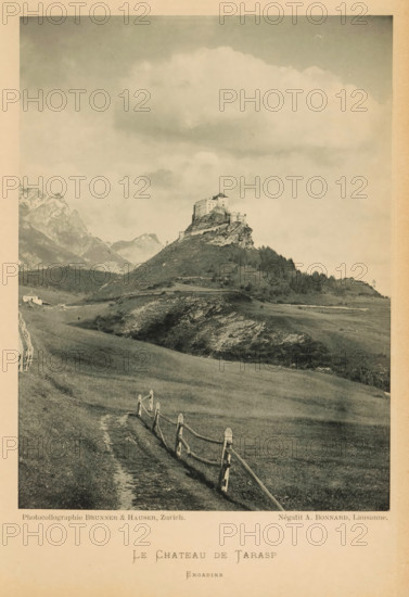 View of a castle in Tarasp, Le Château de Tarasp, page, photomechanical print, photographer: A. Bonnard, maker: Brunner & Hauser, c. 1887 - in or before 1892, paper, collotype, photoprint, height 159 mm x width 119 mm, landscape with tower or castle, (high) hill, A sepia-toned photograph showing a hilltop fortress perched on a rocky outcrop surrounded by rolling grassy slopes and scattered trees, with a winding dirt path and a wooden split-rail fence leading up toward the hill, distant jagged mountains visible on the left, a small building near the base of the hill, and a sky filled with large soft clouds.