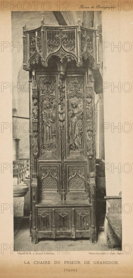 Pulpit, La chaire du prieur de grandson, page, photomechanical print, photographer: MA Vautier, cliché maker: Jules Royer, c. 1887 - in or before 1892, paper, collotype, photoprint, height 201 mm x width 91 mm, ambo, chancel, A tall intricately carved wooden chair or pulpit with ornate gothic detailing fills the frame, featuring a canopy with pointed arches and openwork tracery, carved figures and foliage motifs on the upper panels, and two central vertical panels each containing a carved standing figure within arched niches; flanking columns and side panels bear additional sculpted figures and decorative patterns, the lower section has arched carved panels and a bench-like base, and the piece stands on a stone floor with parts of surrounding stone architecture and seating visible at the sides.