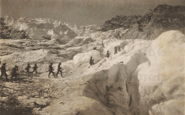 View of Alpine hunters in the mountains in Pelvoux, La 2nne du 30nne chasseurs alpins in the massif du pelvoux (dauphiné), page, photomechanical print, maker: Service photographique du 30nne Bataillon Chasseurs alpins, maker: Richard Paulussen, c. 1890 - in or before 1895, paper, photoaquatint, height 119 mm x width 189 mm, the soldier, the soldier's life, mountains, Pelvoux, Massif du, A sepia-toned mountain scene showing a group of people wearing dark clothing and carrying long poles as they move across a rugged, icy landscape with large snow and ice formations, deep crevices, and uneven frozen surfaces, with rocky mountain slopes rising in the background under a mostly clear sky.