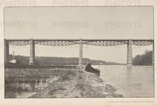 Pont sur l'Isar, View of a bridge over the river Isar, page, photomechanical print, Isar, cliché maker: Meisenbach, Riffarth & Cie., Munich, c. 1892 - in or before 1897, Meisenbach, photographer, cliché maker, Bavaria, paper, autotypie, height 115 mm x width 189 mm, river, bridge, A wide river scene with a long metal bridge spanning across the water supported by tall stone piers, a shoreline in the foreground with rocky ground and sparse grass, a small boat pulled up on the shore partially covered by a dark tarp, distant tree-covered banks on both sides of the river, and a calm water surface reflecting parts of the bridge and surrounding landscape.